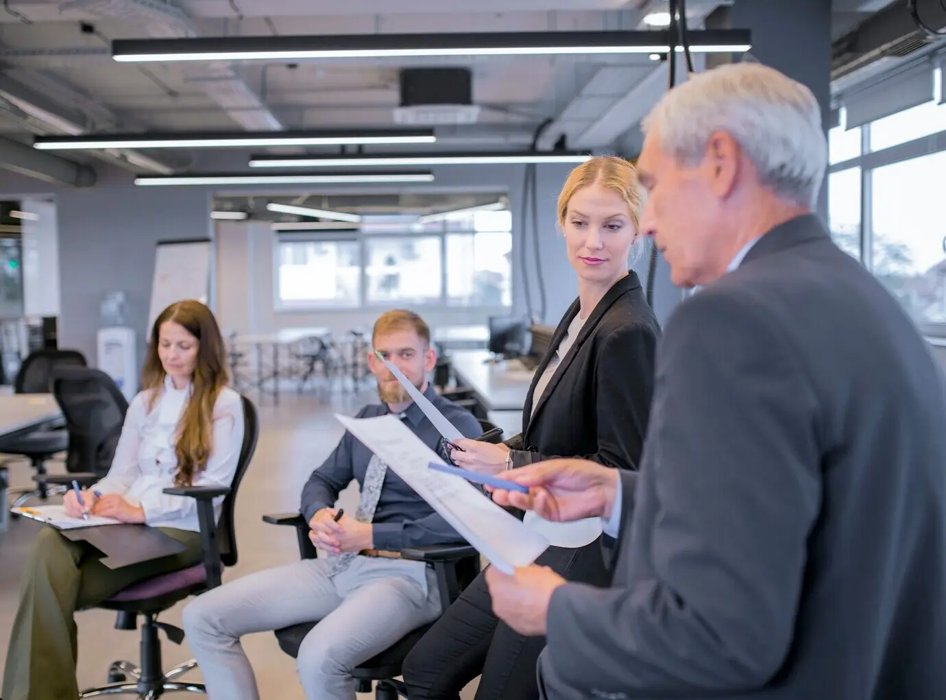 Junge Geschäftsfrau schaut einen älteren Geschäftsmann an, der auf die Dokumente in seiner Hand zeigt.